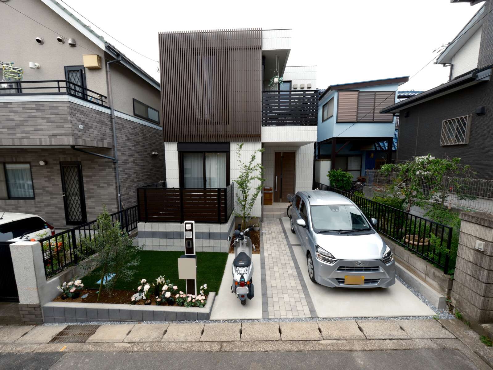 木調フェンスとブロックで囲んだウッドデッキを中心に、駐車スペースやバイク置き場、アプローチ、人工芝や花壇などを取り入れたコンパクトな外構現場の外観