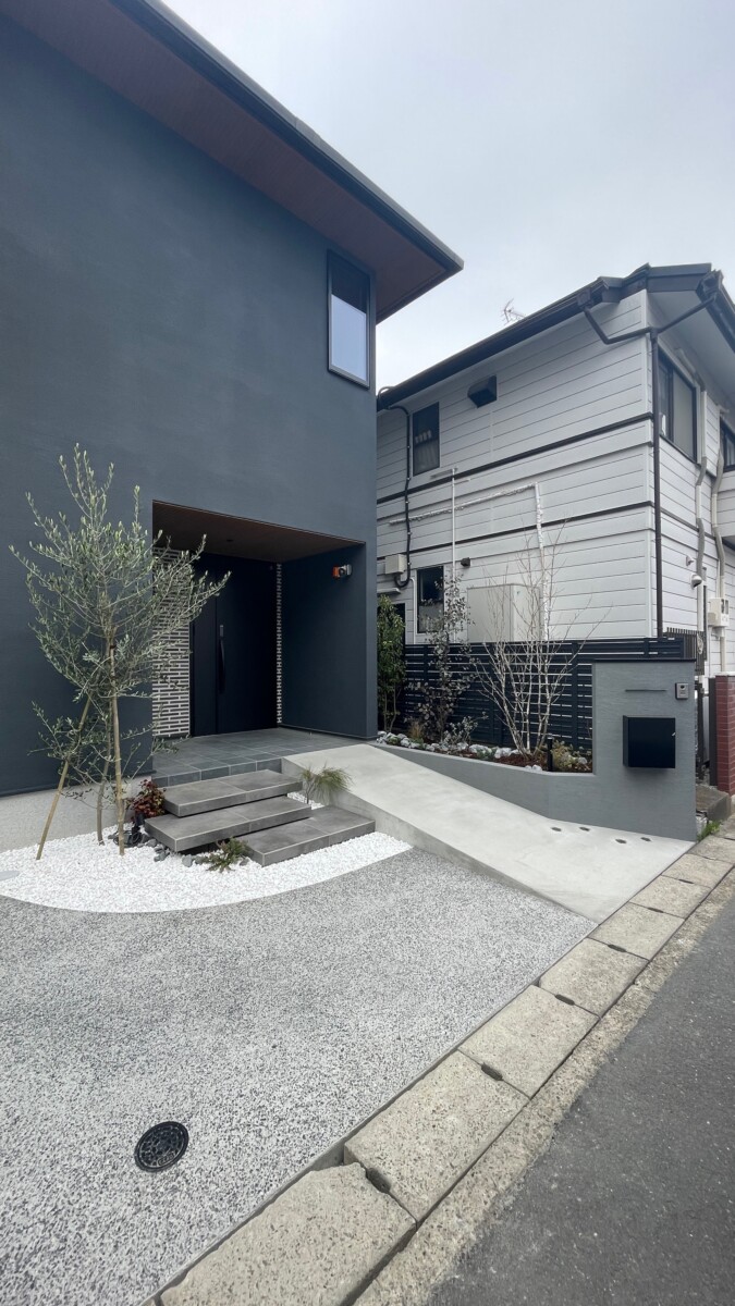 スロープ横に設置された、質感のある塗り壁仕様の門柱と緑豊かな花壇