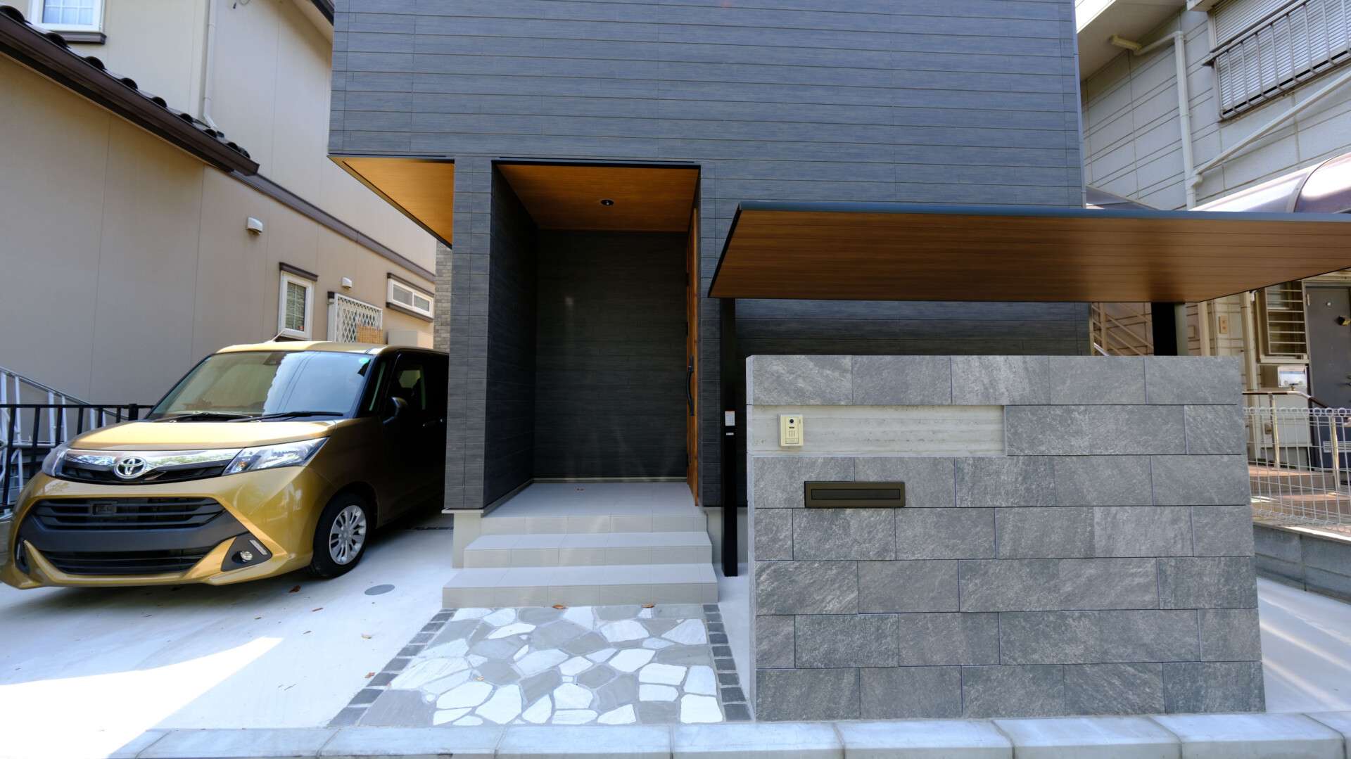 富士見市の新築外構。タイル門柱と自然石アプローチの門まわりと玄関ドアと調和した木目調テラスSC