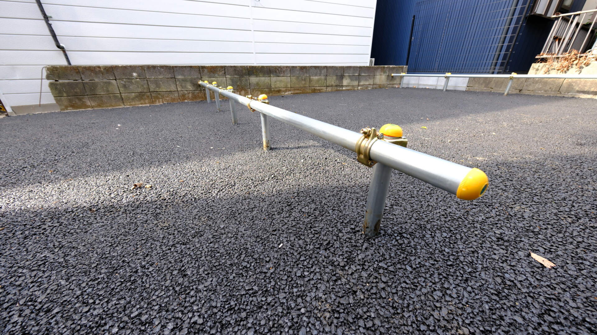 アスファルトの上に設置された安価で機能的なゴム製の車輪止めと単管パイプの支柱。