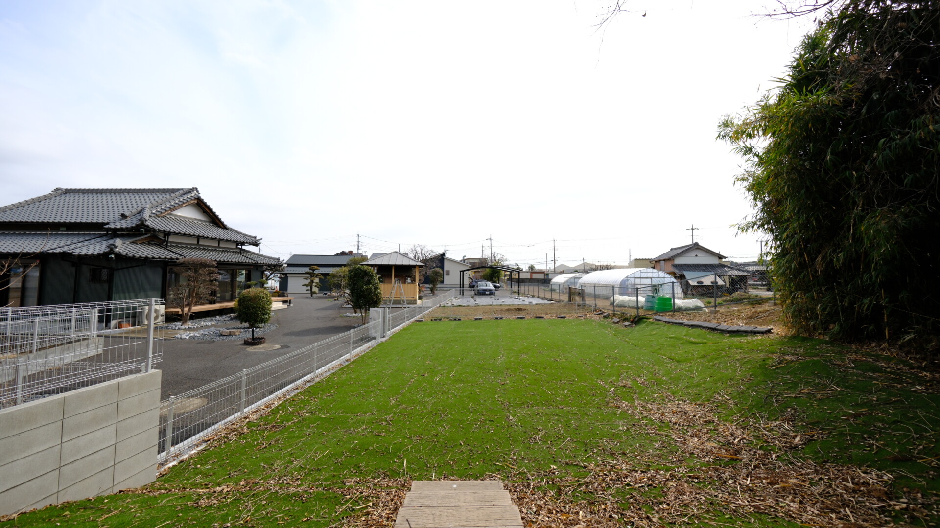 広大な敷地一面に防草シートと人工芝を敷き詰めたメンテナンスフリーな庭と敷地の全景