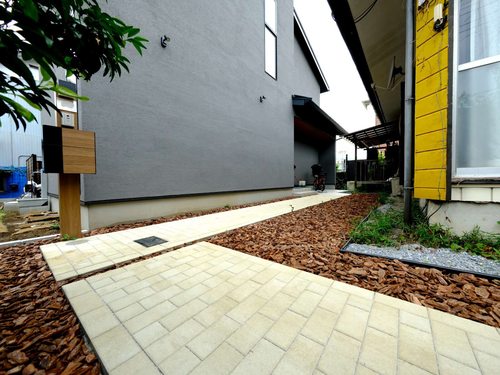 モダンな建物に合わせたインターロッキングのかぎ型アプローチと木目調の機能門柱がおしゃれな新築外構写真