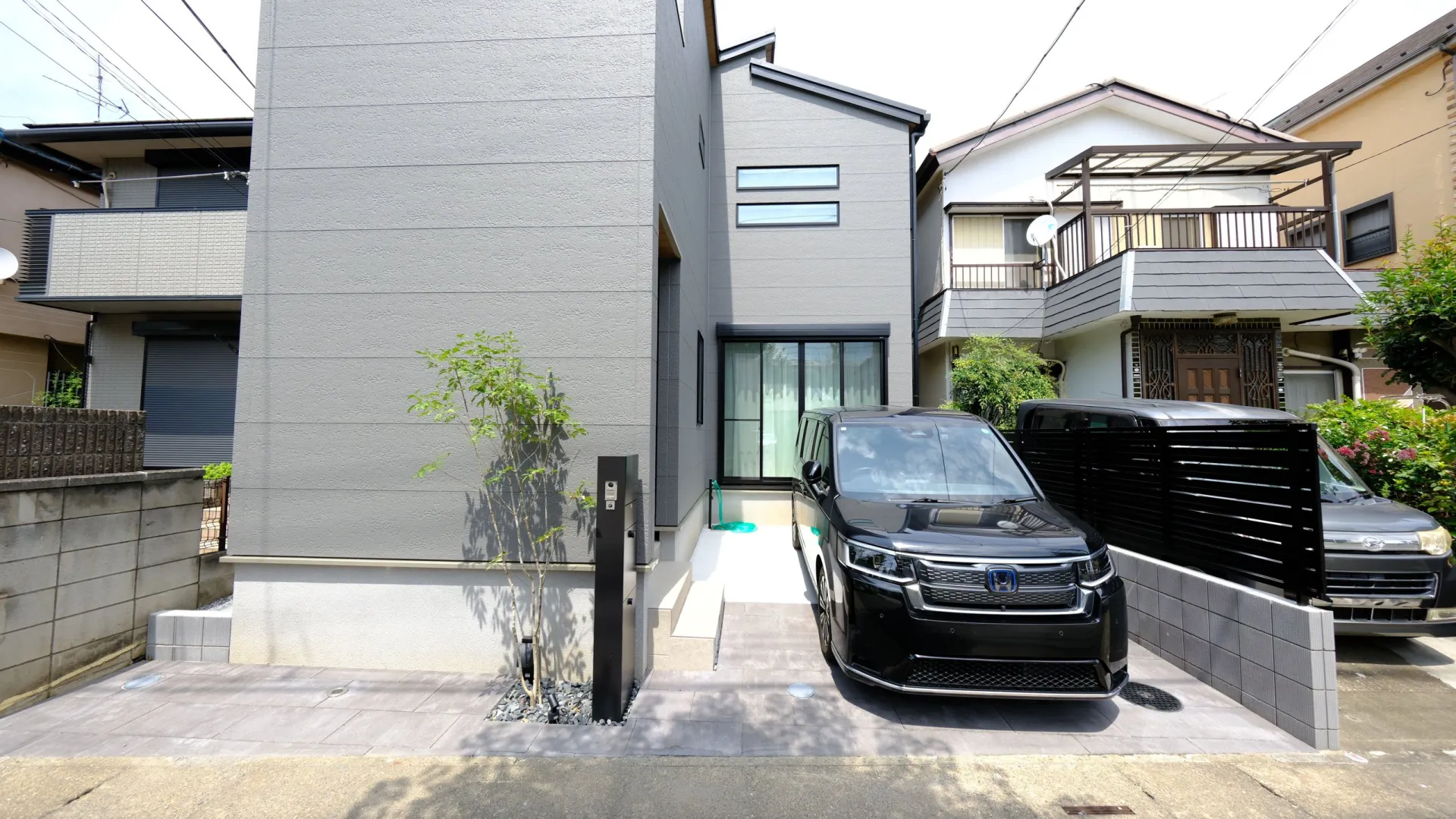 大判のコンクリート平板を敷いた駐車スペースとアプローチ、黒の目隠しフェンスでまとめた新築外構の外観(川口市)