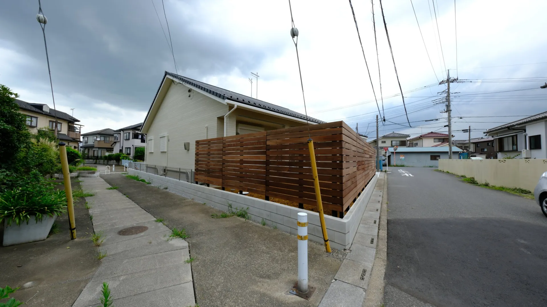 広い敷地の角地に沿って続く天然木フェンスと施工後の外構全体（越谷市）