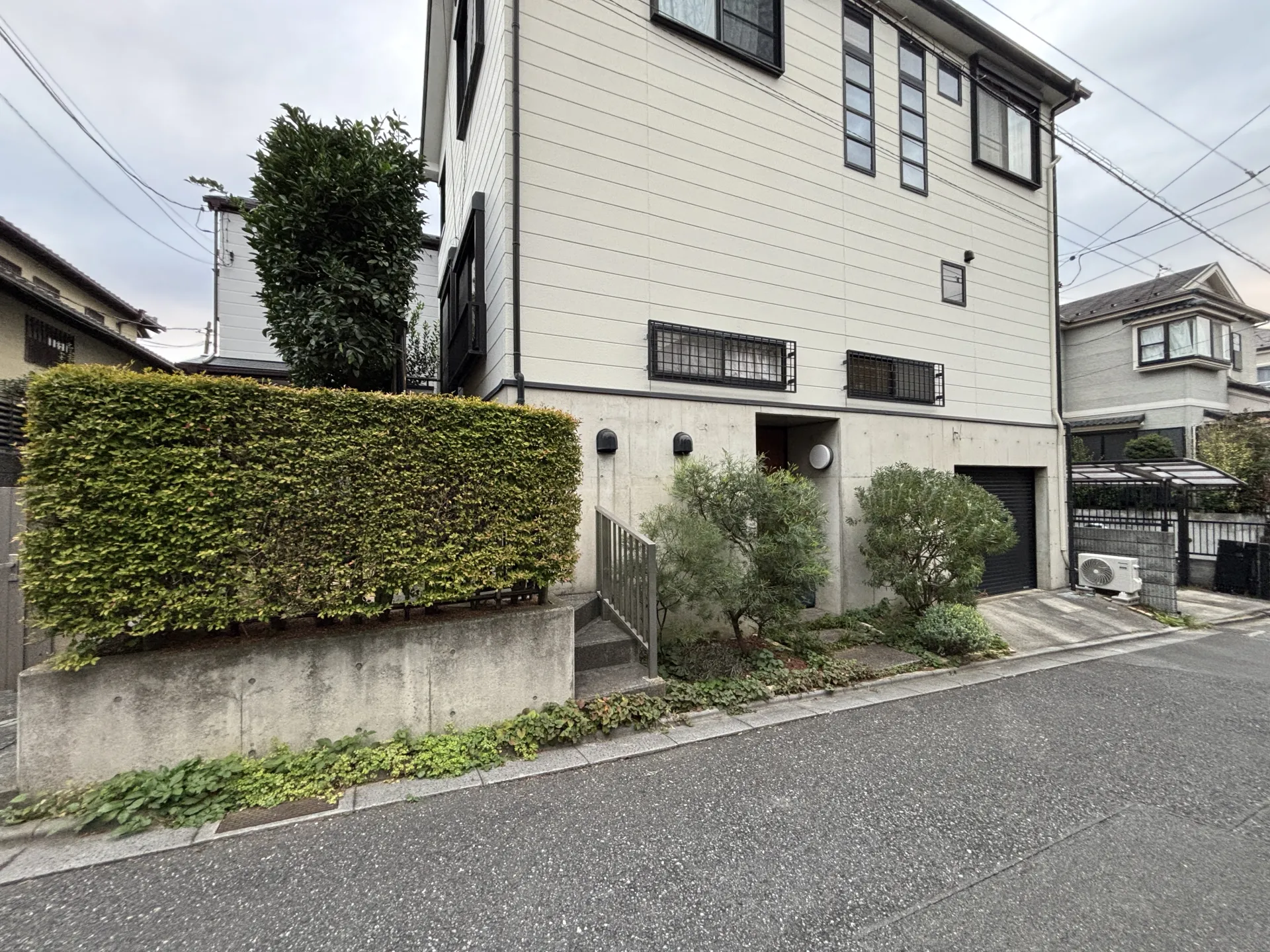 施工前のさいたま市緑区の戸建て外構。道路側に生け垣が植えられ、建物全体がやや重たい印象になっている状態。