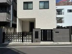 新築クローズ外構の門まわり全景。親子門扉と大判タイル門柱、スマート宅配ボックスが配置された防犯性の高いエントランス。