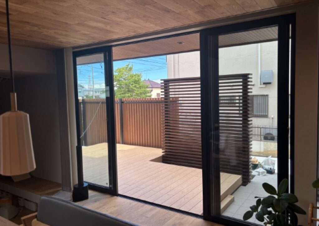 室内のフローリングと質感を揃えた人工木デッキと縦格子の目隠しフェンス